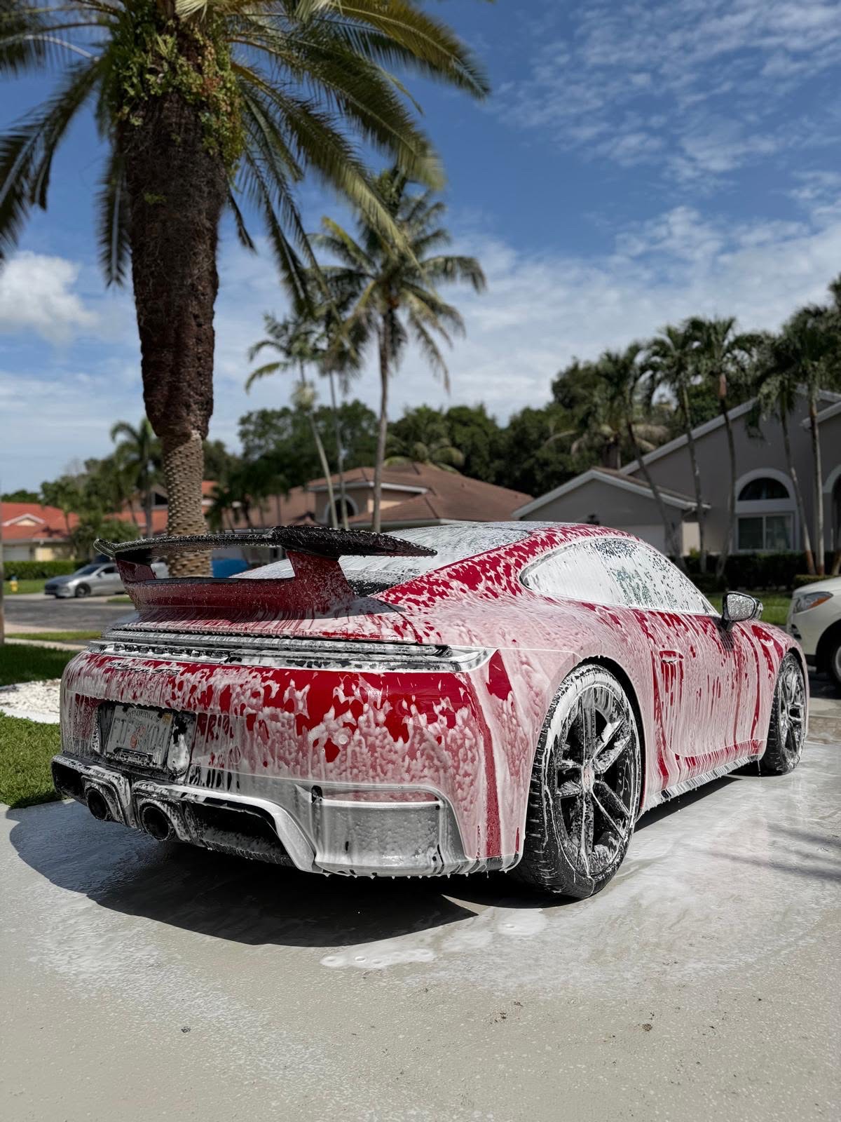 Red Porsche 911 GTS rear covered in snow foam under palm trees