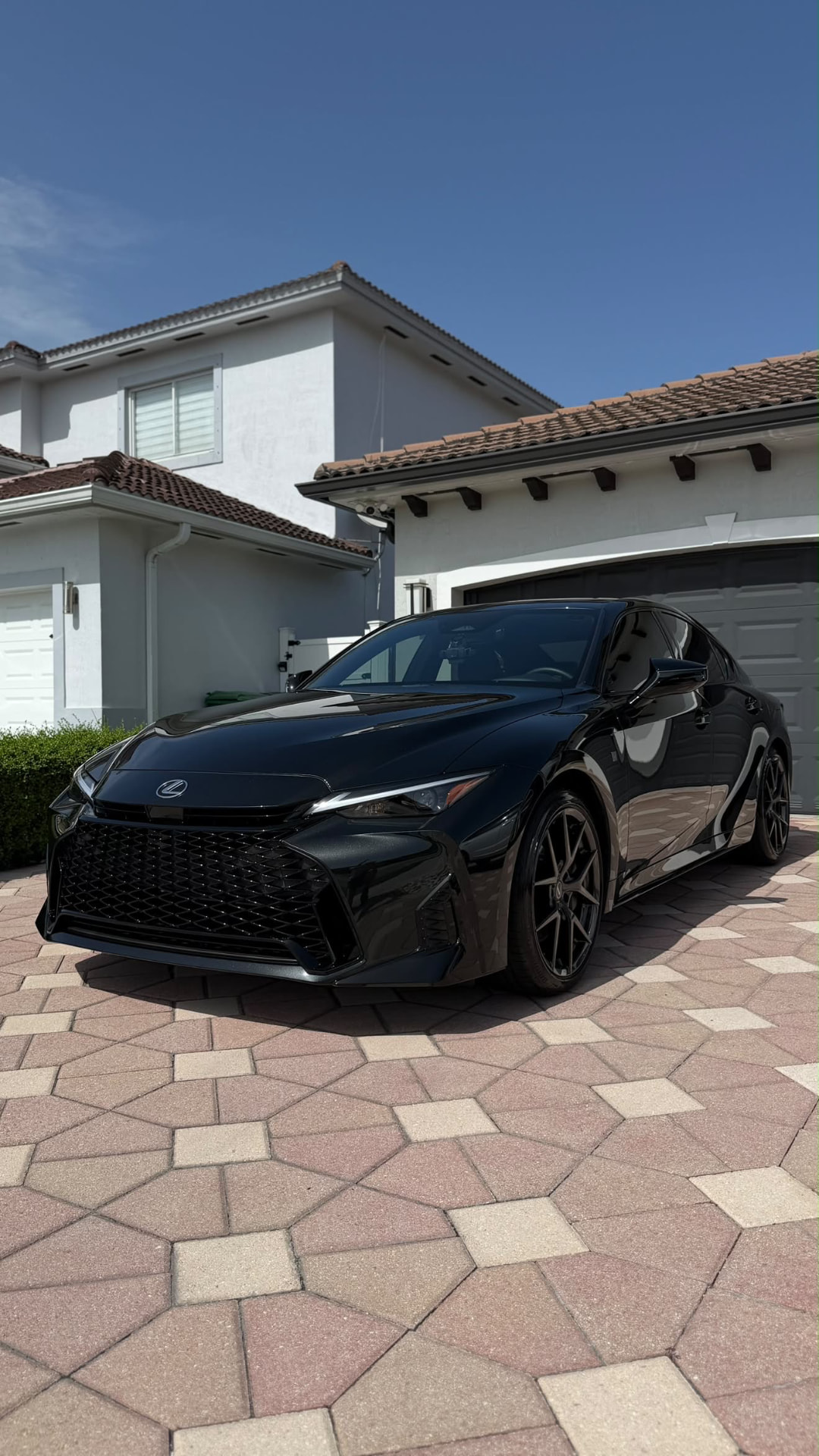 Black Lexus IS glossy on a paver driveway in front of a Miami home
